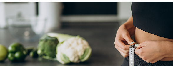 Hands measuring waist near vegetables